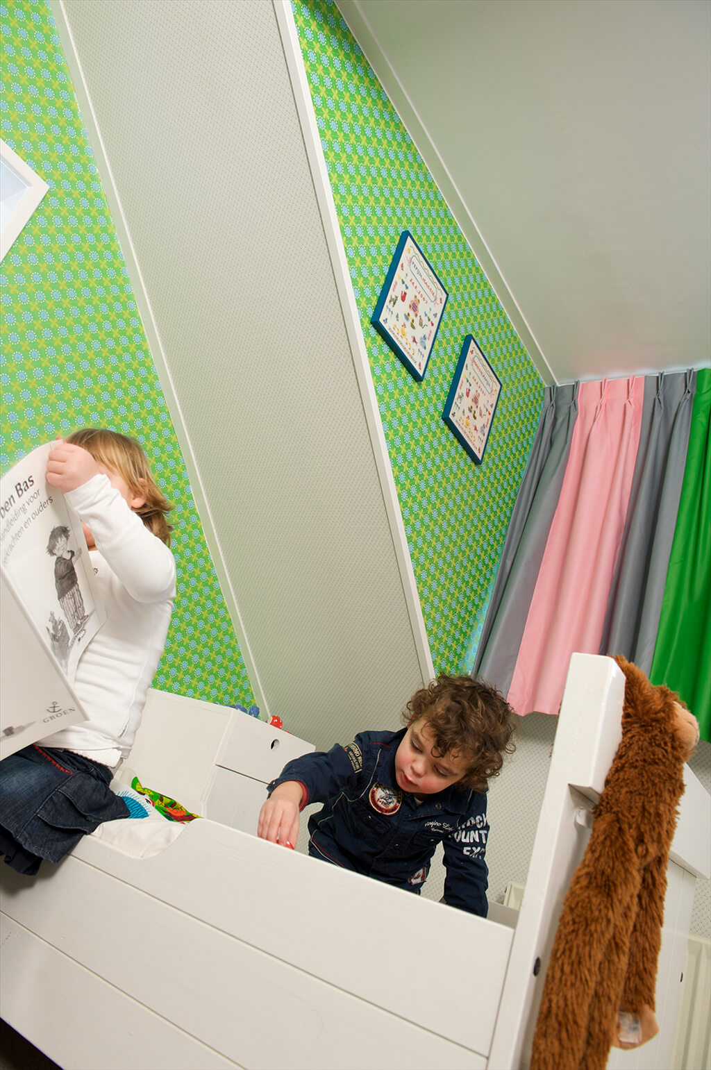 Spielende Kinder auf dem Boden und Bett mit einer mehrfarbigen Gardine im Hintergrund