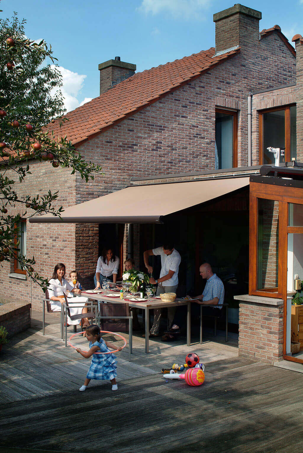 Familie und Freunde beim Essen auf der großen Terrasse unter der braunen Markise